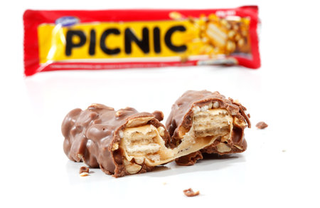 A Cadbury Picnic chocolate bar 46g (1021kj).  Showing wrapper packaging in background and chocolate bar contents in focus in the foreground. Picnic contains nuts, wafer, chocolate, rice crisps and caramel.  Photographed in studio on a white background.のeditorial素材