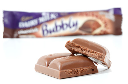Cadbury Dairy Milk Bubbly 40g (892kj) Dairy milk chocolate with a light bubbly light aerated centre. Showing packaging in background and pieces of the chocolate in focus in the foreground.  Photographed in studio on a white background. のeditorial素材