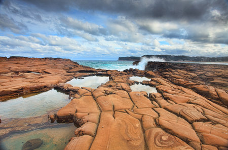 Ocean waves splash against spectacularrock formations at North Avoca, NSW Australia, with serene rockpools in the foreground   の写真素材