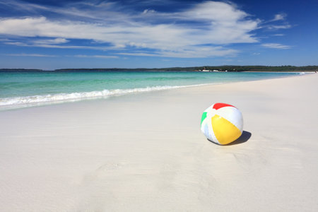 A colourful beach ball on the sand by the beach with space for your message.
