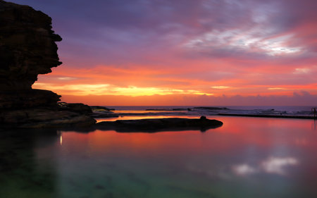 A long exposure at dawn captures the beautiful colours in the sky and reflections in the rock pool against silhouetted rock cliffs.  North Curl Curl Australia.の写真素材