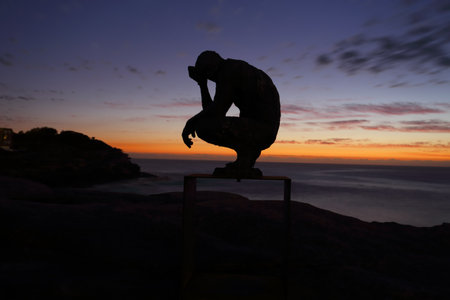 BONDI, AUSTRALIA - OCTOBER 25, 2015;  Annual Sculpture by the Sea free public event.  Exhibit titled Crouching Man by Laurence Edwards.    Made of bronze. Silhouette against dawn skyのeditorial素材