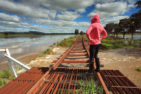 A female looks out over the floodwaters from the buckled train tracks at Crowther, Hilltops Region, Country NSW.の写真素材