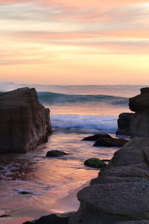 Beautiful colours in the wispy wind swept sky and tidal waves wash in between rocks on the beachの写真素材