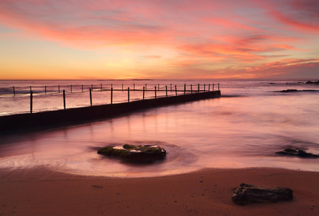 Red skies and vivid colours of dawn at Newport Beach ocean rock poolの写真素材