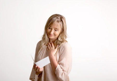 Woman reading a heartfelt message, note, book or card.   She is smiling and has her hand to heart. White backgroundの写真素材