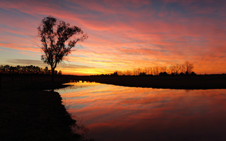 Spectacular sunrise with fiery skies and colourful hues reflected in the water and contrasted...