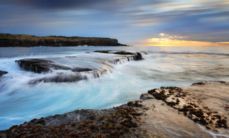 Fast flowing ocean waves over and around rocks in the low tide at Little Bay Australiaの写真素材