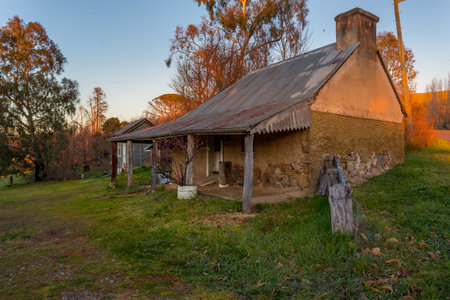 Rustic old farm house with its render exposing what looks like hand cut irregular shaped stones that formed the walls of the building with many gaps and felled tree trunks to hold up a verandah.の写真素材
