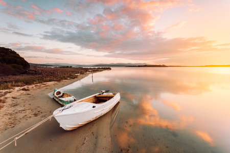 Old boat moored on sandy shore with sunrise reflectionsの写真素材