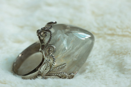 A well-polished quartz pebble on a silver ring that is decorated with tree leaves.の写真素材