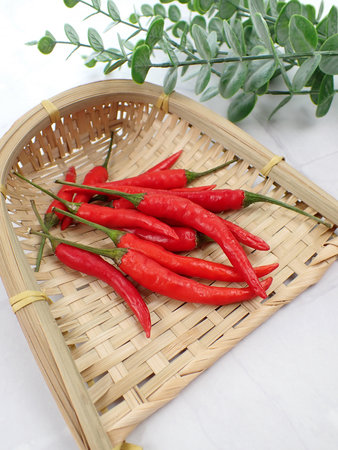 Spicy Food Ingredient Red Hot Chili Chilli Chillies Pepper Peppers in a Bamboo Rattan Basket on a White Marble Table Backgroundの写真素材
