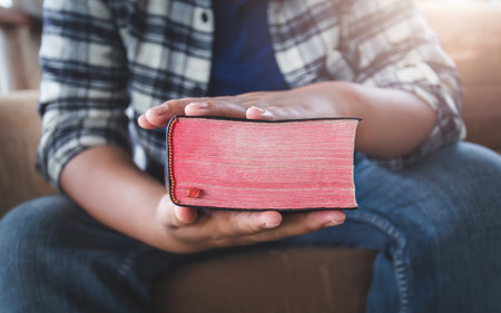 Close up hands of man holding a red bible on sofa at home. christian concept.の写真素材