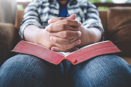 Close up hands of young male praying on bible at home. Christian prayer concept.の写真素材