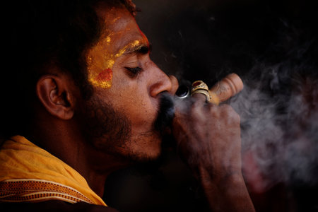 Varanasi / India - Mar 02 2013 : Young yogi priest smokes and closes his eyes. The hand holding a...