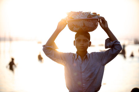 Varanasi / India - Mar 02 2013 : The boy wore a shirt and placed a basket of offerings on his head. He was at the Ganges in the afternoon.  The sunlight coming from the back makes a black silhouette.のeditorial素材