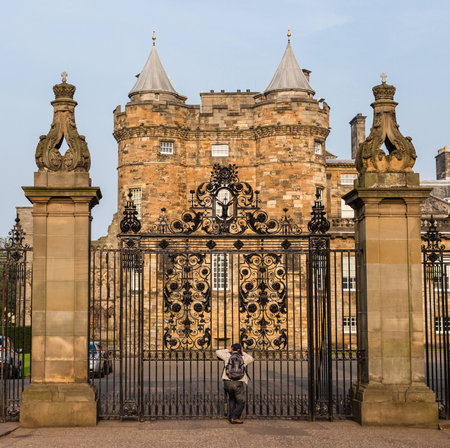 An eager tourist takes pictures from the closed main gates of the Palace of Holyroodhouse, located at the East end of The Royal Mile in Edinburgh, Scotlandのeditorial素材