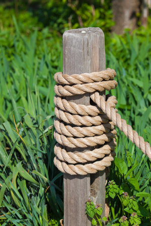 This is a photo of a post with a rope coiled around it  Green grass is in the background の写真素材