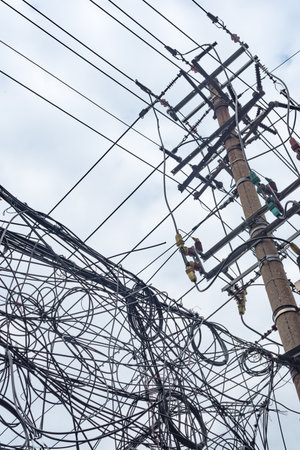 Telephone pole and chaotic mess of wires against skyの写真素材