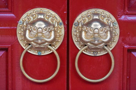 Golden colored chinese door knockers on a red door in Chinaの写真素材