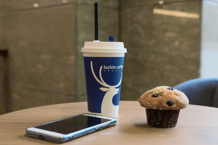 Chengdu, Sichuan province, China - Dec 14, 2018 : Luckin coffee cup with muffin and smartphone on a tableのeditorial素材