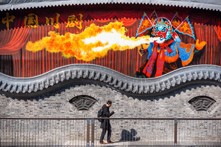 Chengdu, Sichuan province, China - Feb 3, 2019: Man walking by a brick wall with a painted fresco of a fire spitter chinese opera artistのeditorial素材
