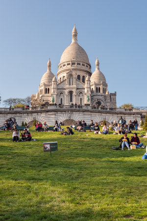Paris, France - April 12, 2019 : People sitting on the grass in front of the Basilica of the Sacre Coeur in the hill of Montmartre on a sunny dayのeditorial素材