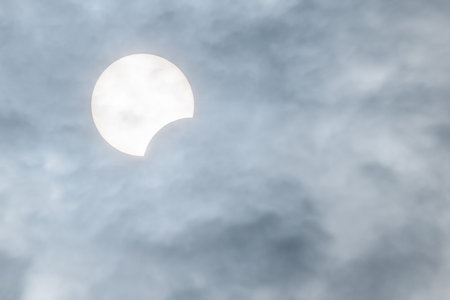 Partial sun eclipse behind clouds