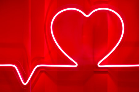Red neon heart shape and heartbeat line on metal wall close-up viewの写真素材