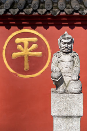 Chengdu, Sichuan province, China - Sept 28, 2021 : Soldier sculpture in front of the red surrounding wall of Wenshu buddhist monastery with the chinese character - ping- meaning peace.のeditorial素材