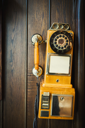 Old vintage rotary telephone hanging on a wooden wall close-up view
