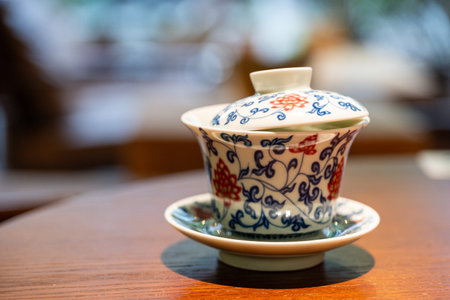 A tea cup sits on a wooden table in a restaurant in Chengdu, Sichuan. The cup has intricate designs and is part of the local dining experience. This moment captures cultural heritage.の写真素材