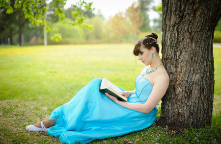 Girl sitting with book near treeの写真素材