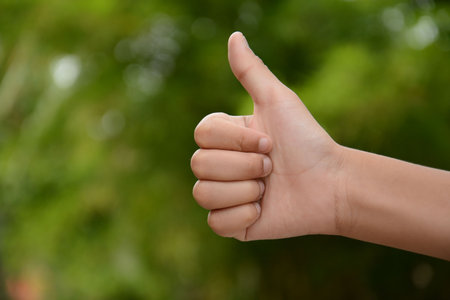 Hand with thumb up on nature bokeh background. Ok sign by womanの写真素材