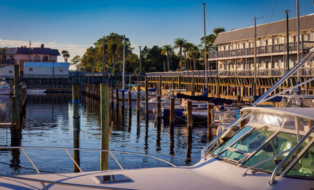 A boat is docked at a marina with several other boats in the water. The scene is calm and peaceful, with the sun shining brightly overhead. The marina is located near a townの写真素材