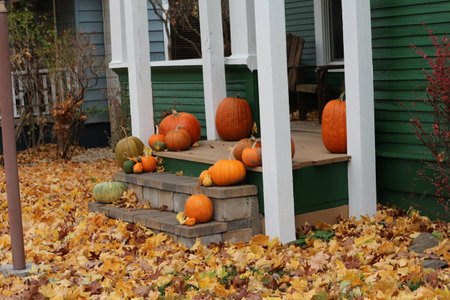 A crisp fall day with fallen leaves on a lawn and a porch decorated with pumpkins gives mood of coming halloween.の写真素材