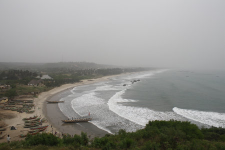 A coastal view from Fort Amsterdam, Ghana, featuring a sweeping panorama of the ocean meeting the sandy shore, dotted with fishing boats and a distant villageの写真素材