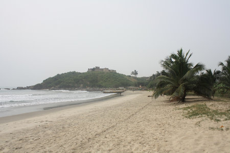 A vibrant coastal scene with an abandoned wooden boat marked "STILL" resting on the sandy beach, with lush greenery and a historic fort in the backgroundの写真素材