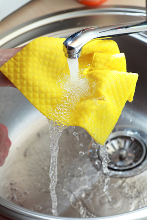 yellow cloth and hands under running water の写真素材