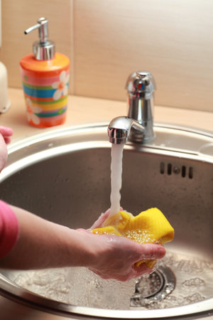 yellow cloth and hands under running water の写真素材