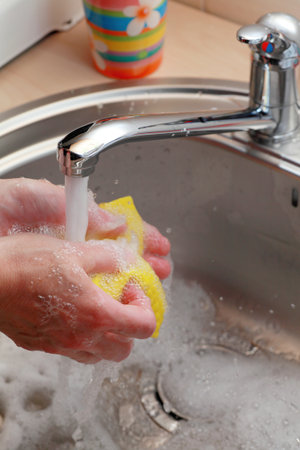 hands holding yellow cloth under running water の写真素材