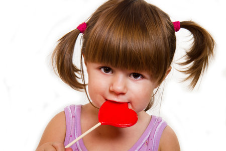 little girl eating red heart lollipop isolated on whiteの写真素材