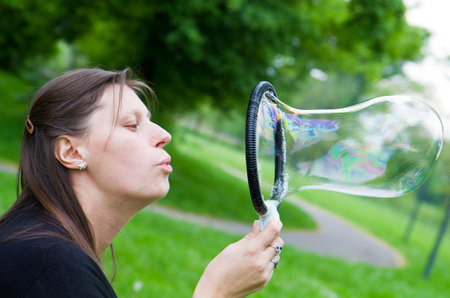 woman inflating colorful soap bubbles in spring park の写真素材