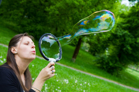 woman inflating colorful soap bubbles in spring park の写真素材