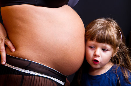 Child kissing belly of pregnant woman against black backgroundの写真素材