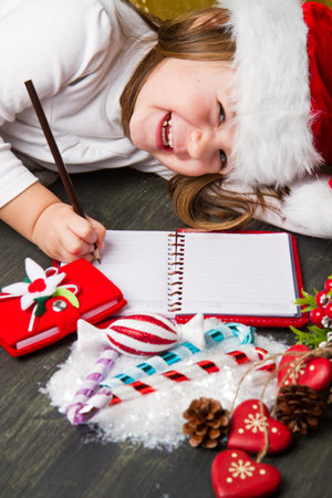 Funny girl in Santa hat writes letter to Santa near christmas decorationの写真素材