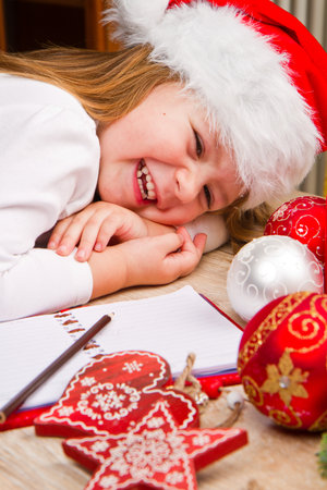 Funny girl in Santa hat writes letter to Santa near christmas decorationの写真素材