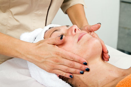 Beautiful young woman receiving facial massage with closed eyes in a beauty centerの写真素材