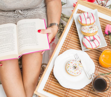 woman having breakfast in bed while reading a bookの写真素材