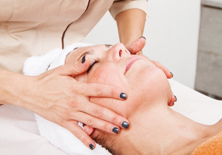 Beautiful young woman receiving facial massage with closed eyes in a beauty centerの写真素材